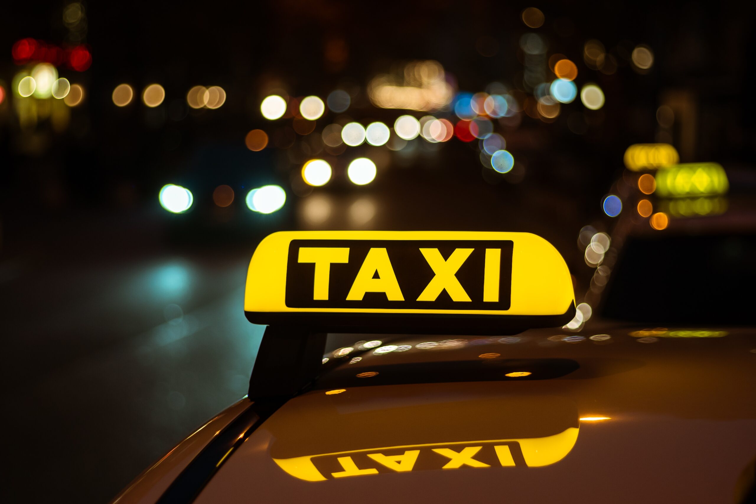 Yellow and black sign of Taxi placed on top of a car at night A yellow and black sign of Taxi placed on top of a car at night
